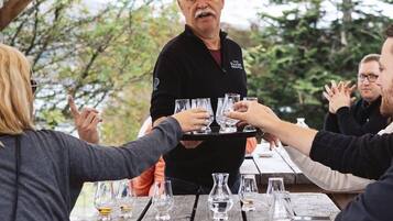 Un grupo de personas en una mesa de madera al aire libre, con vasos y botellas, bajo una estructura de madera.