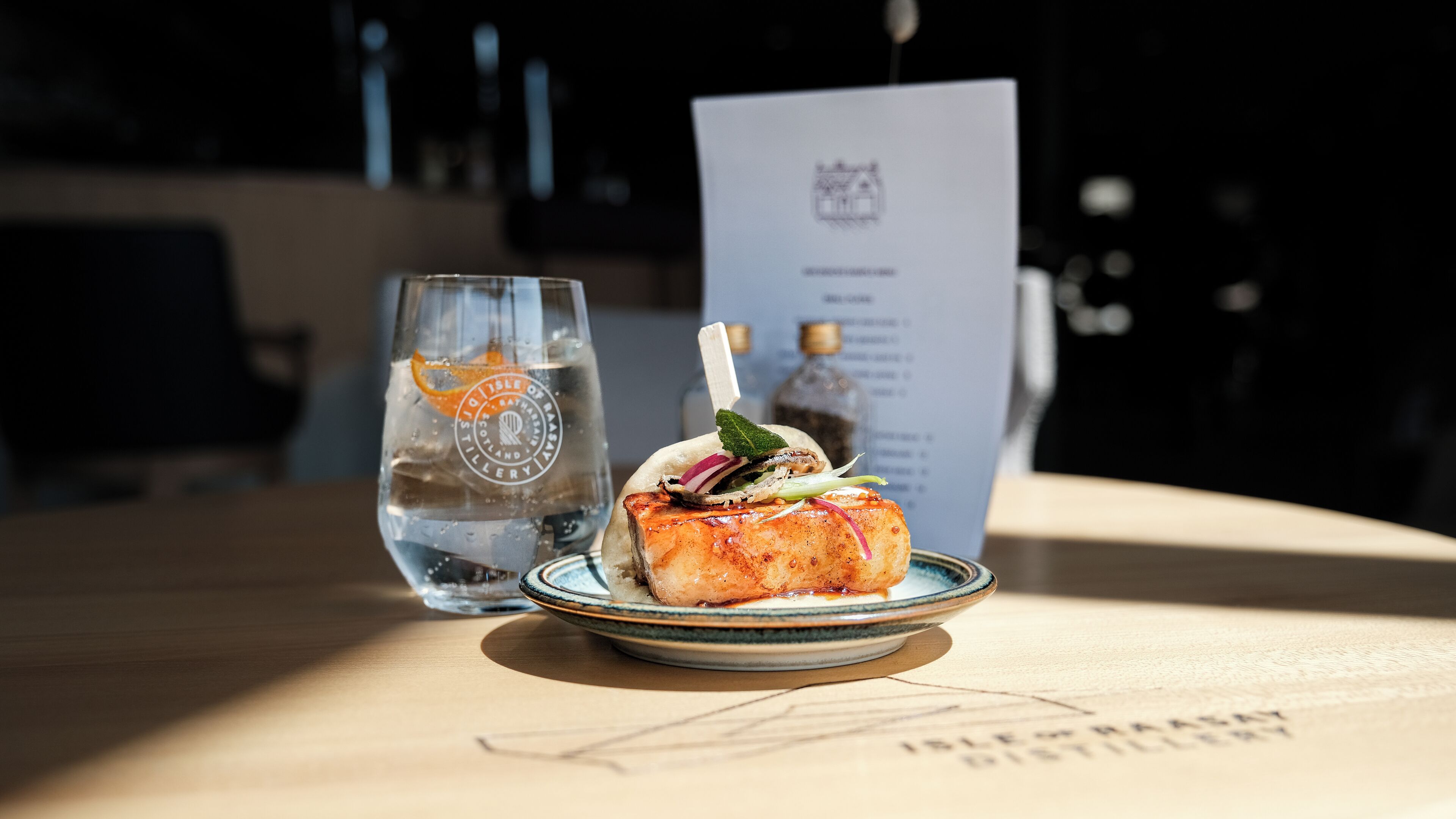 A plate with a piece of grilled fish, a glass of water, and a menu on a table.
