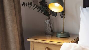 A bedside table with a lamp, a vase with a plant, and a bed with white bedding.