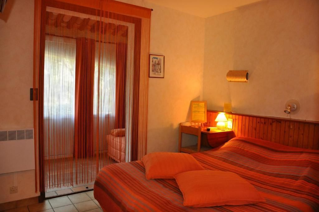 A hotel room with a bed, a nightstand with a lamp, a chair, and a window with curtains.