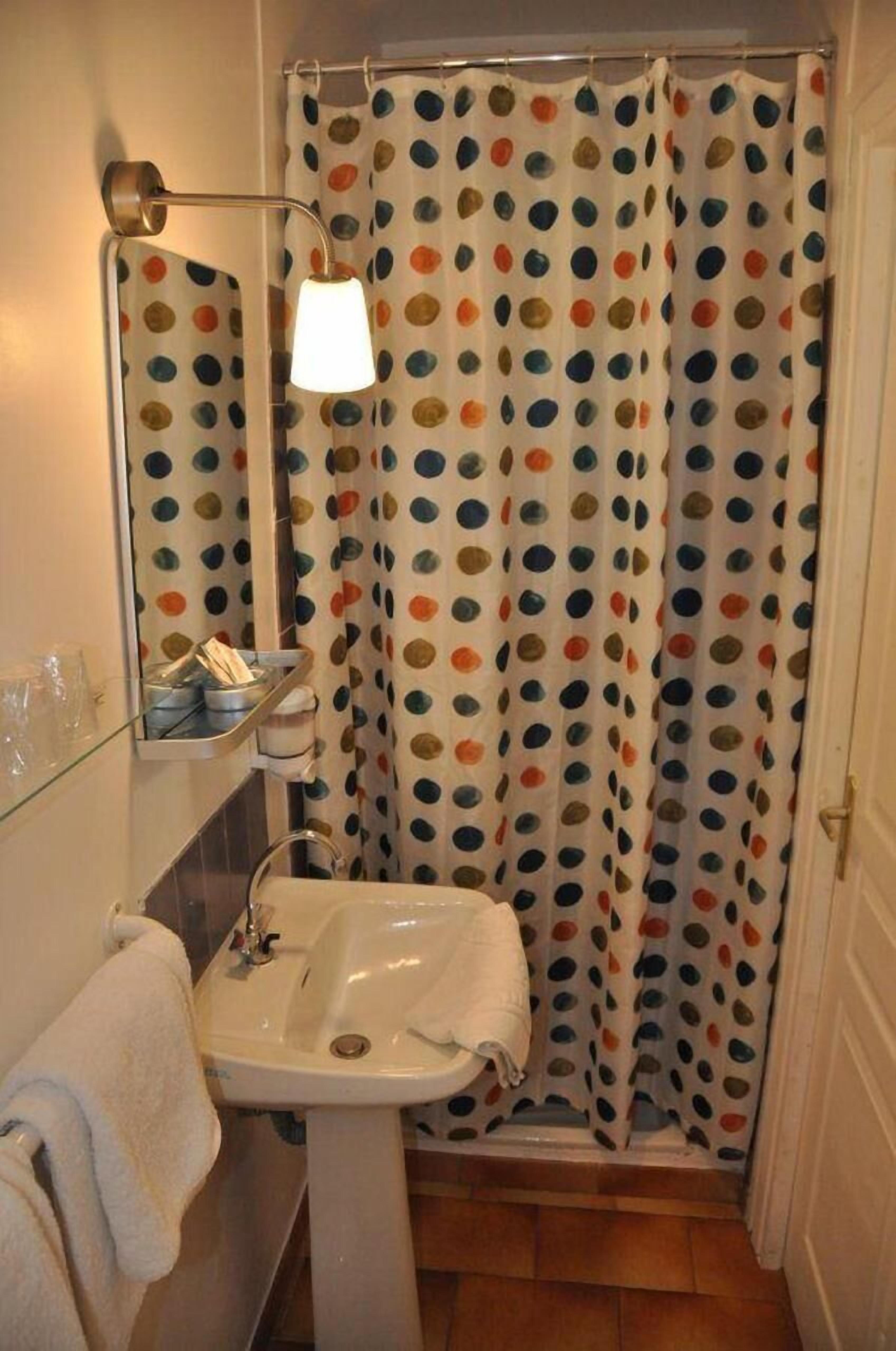 A bathroom with a white sink, a mirror, a shower curtain with a polka dot pattern, and a wall-mounted light fixture.