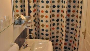 A bathroom with a white sink, a mirror, a shower curtain with a polka dot pattern, and a wall-mounted light fixture.