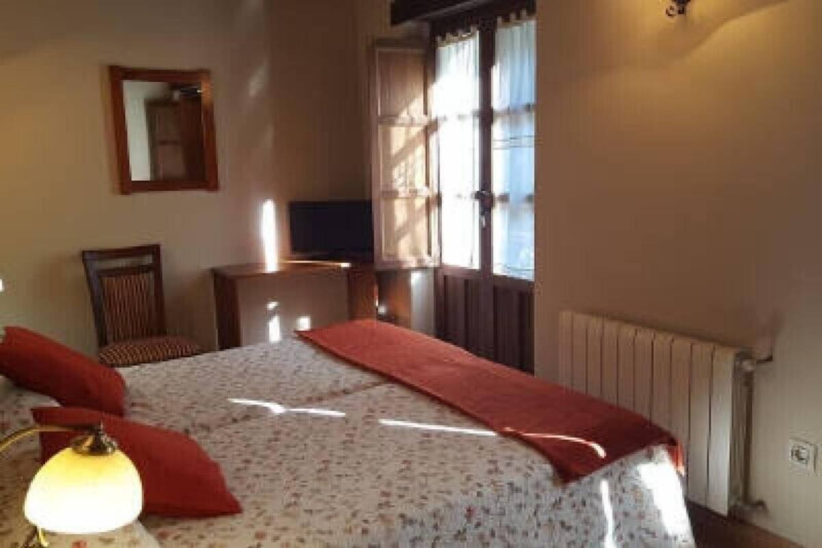 Quarto com cama, cadeira, escrivaninha, televisão e janela com cortinas.