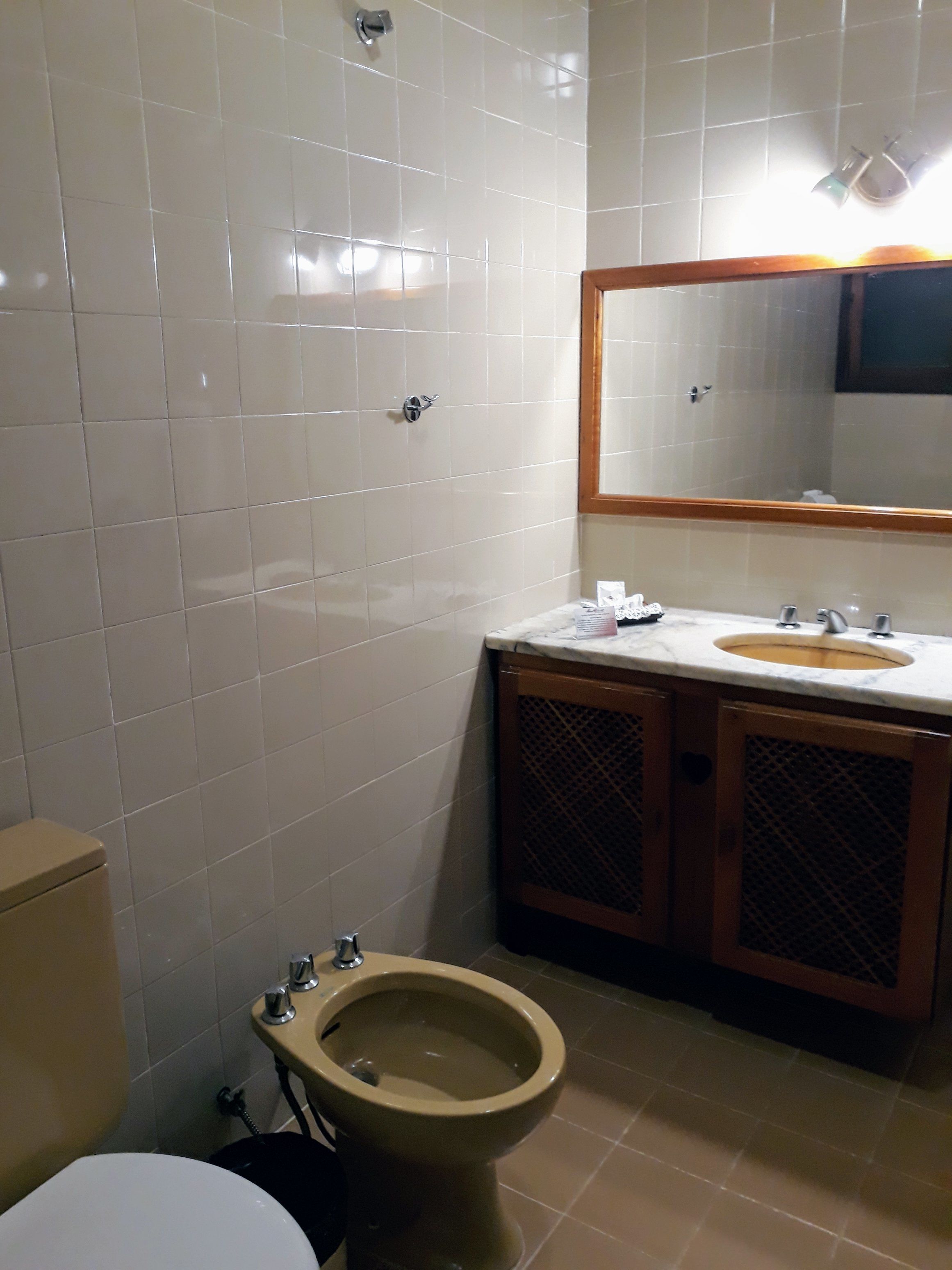 Ein Badezimmer mit weißen Fliesen, einem Holzkosmetikschrank mit Waschbecken, einem Spiegel und einem Bidet.