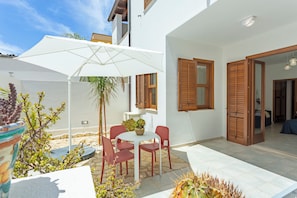Um pátio com mesa e cadeiras, um guarda-sol branco e venezianas de madeira.