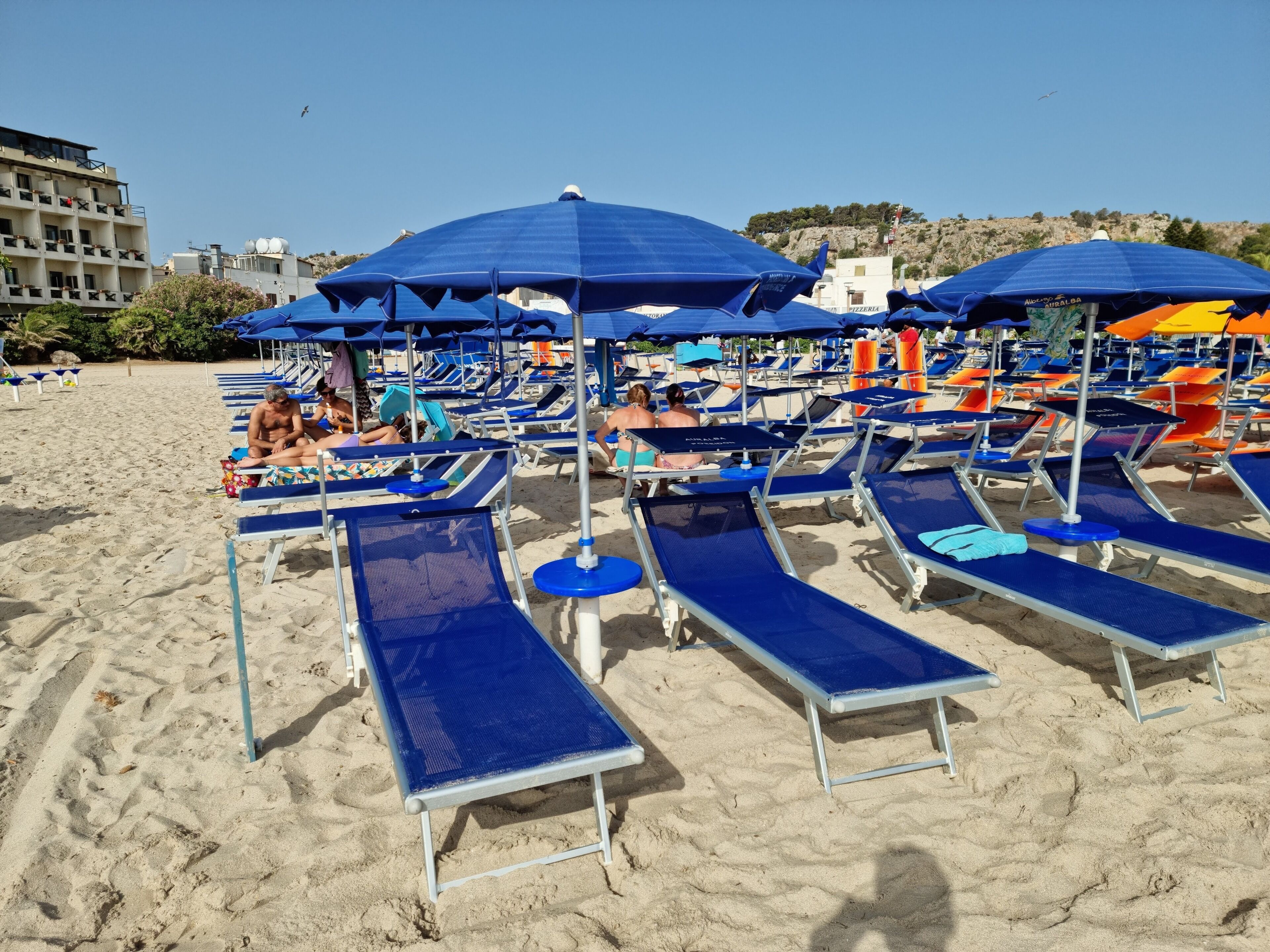 Una playa con filas de tumbonas y sombrillas, algunas ocupadas por gente.