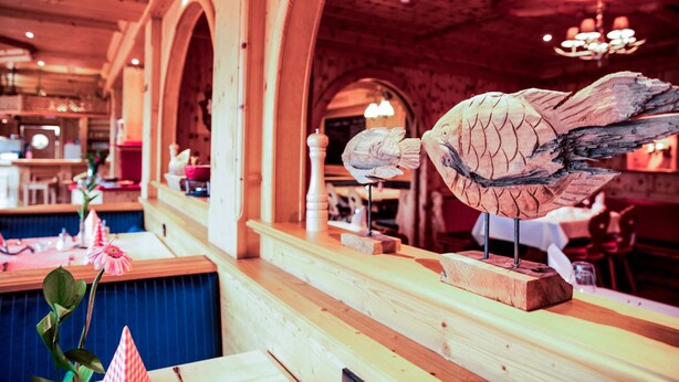 A restaurant interior with wooden arches, a fish sculpture on the counter, and a blue tablecloth. - Jagdschloss Windenhütte (Thale)