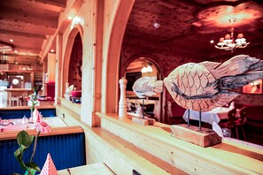 A restaurant interior with wooden arches, a fish sculpture on the counter, and a blue tablecloth. - Jagdschloss Windenhütte (Thale)
