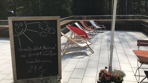 An outdoor seating area with a chalkboard menu, sun loungers, and a large umbrella. - Jagdschloss Windenhütte (Thale)