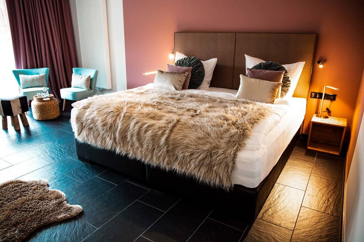 Una cama grande con un edredón mullido, dos sillas, una mesita y una lámpara.