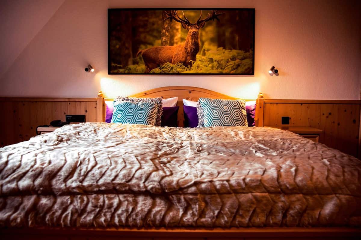 Un dormitorio con una cama grande, almohadas estampadas, un cabecero de madera y un cuadro con un ciervo en la pared.