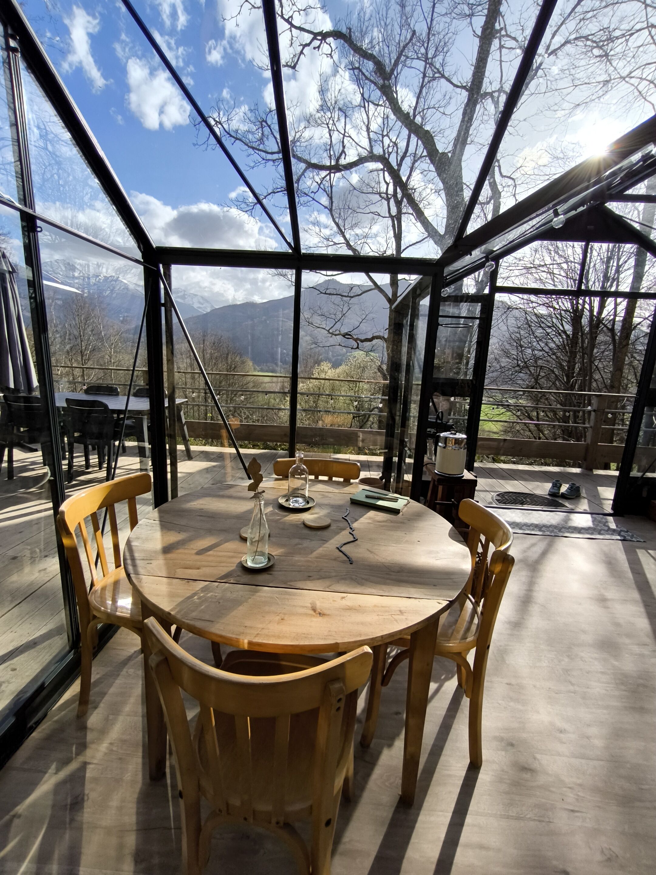 Una mesa de madera con sillas en una habitación con paredes de vidrio y vistas a la montaña.