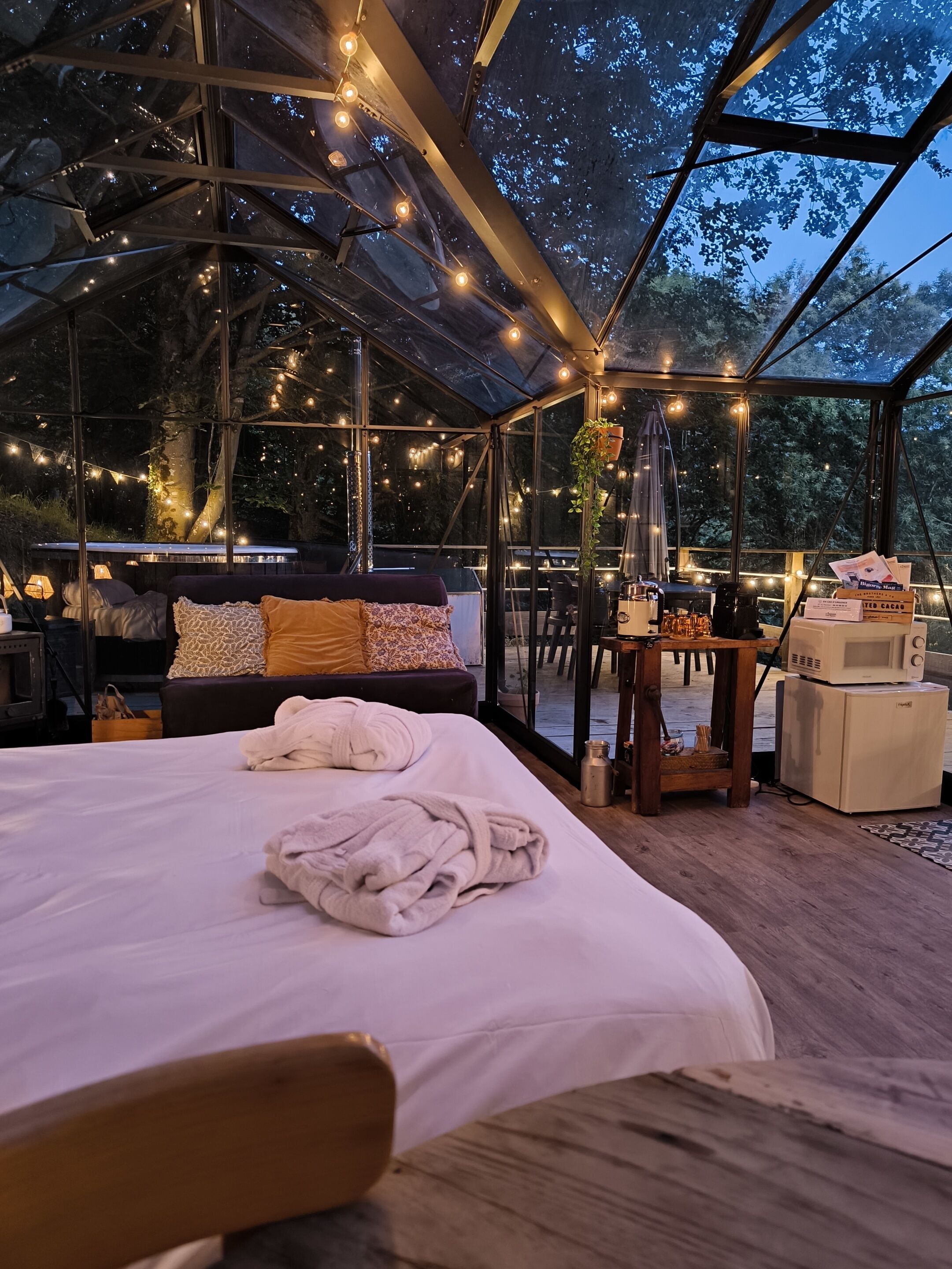 A spacious, well-lit tent with a large bed, a table with a microwave, and string lights.