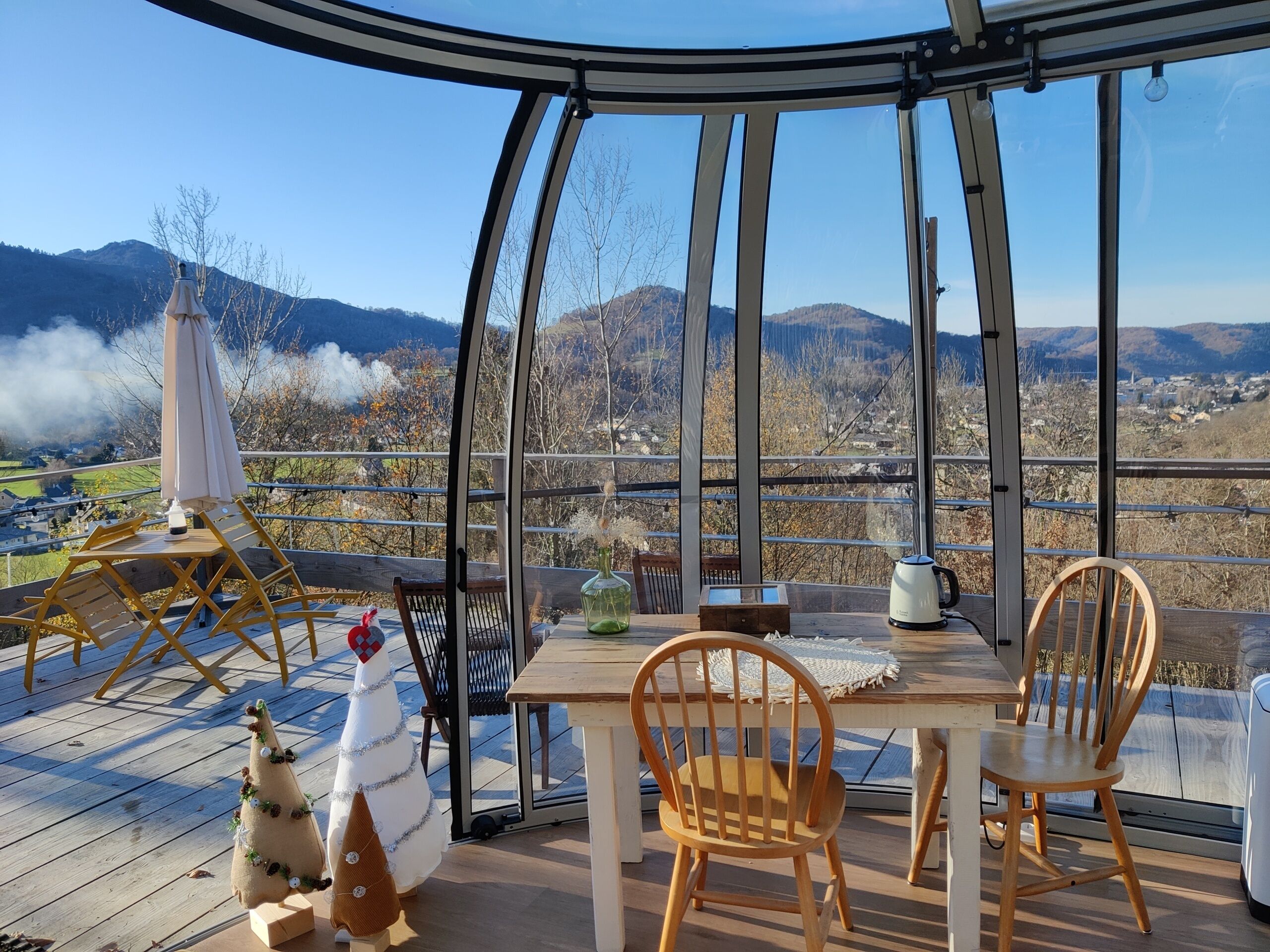 A covered outdoor seating area with a table and chairs, a decorative Christmas tree, and a view of the surrounding landscape.