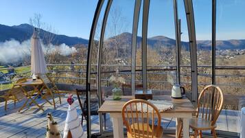 A covered outdoor seating area with a table and chairs, a decorative Christmas tree, and a view of the surrounding landscape.