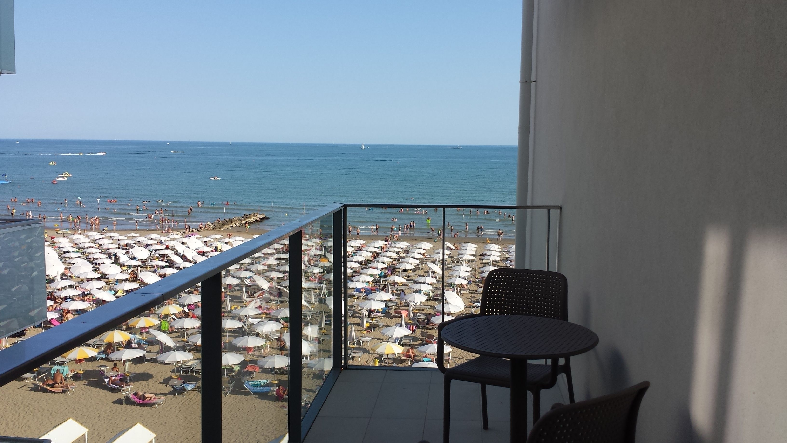 Un balcón con vista a una playa concurrida y al mar.