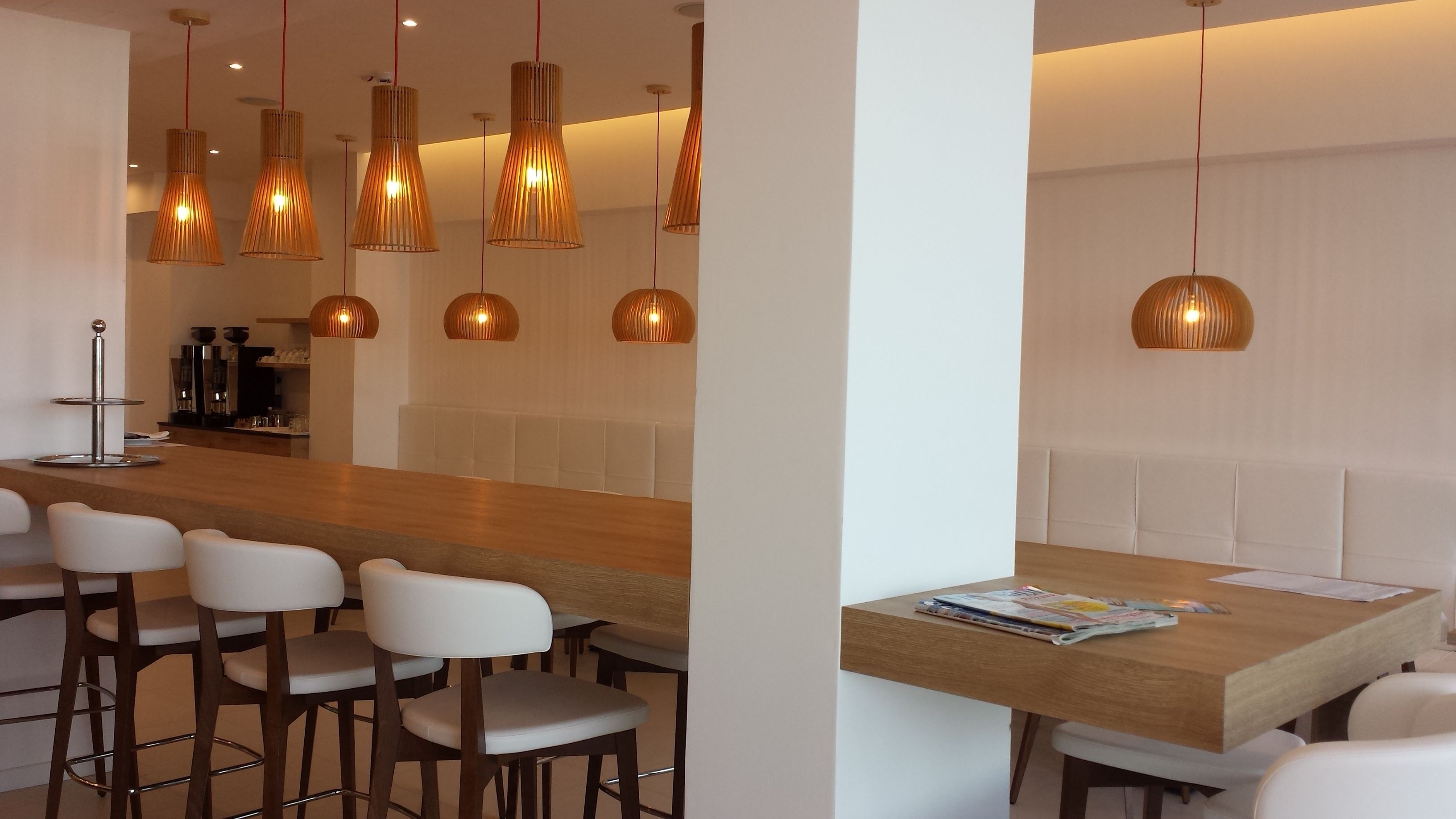 A modern bar area with a wooden counter, white bar stools, and multiple hanging pendant lights.