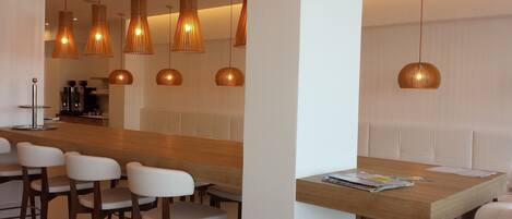 A modern bar area with a wooden counter, white bar stools, and multiple hanging pendant lights.