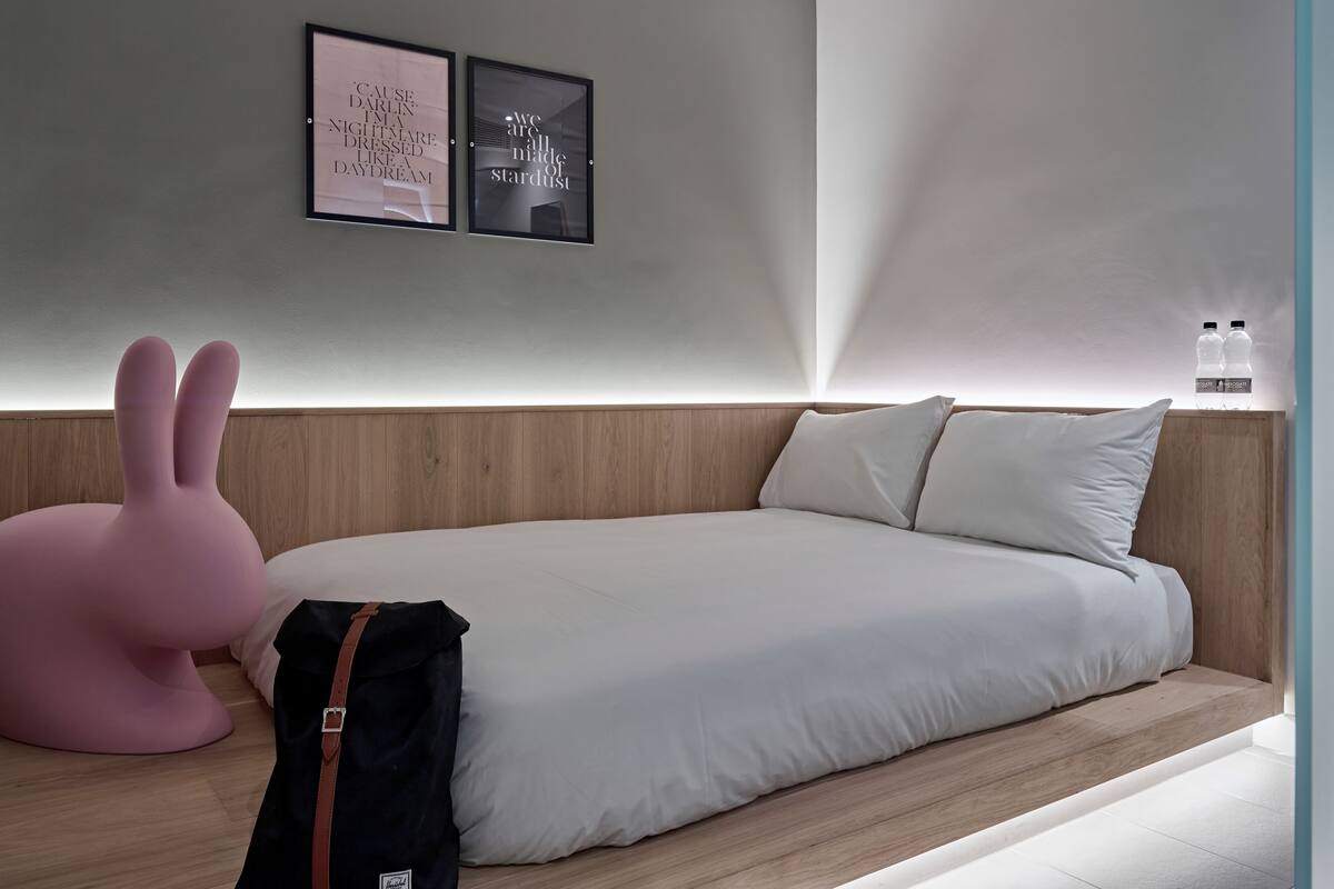 A modern bedroom with a wooden headboard, a large bed, a pink chair, and two framed quotes on the wall.