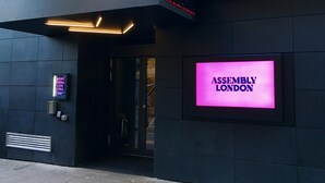 The exterior of a building with a neon sign reading "ASSEMBLY LONDON" and a modern entrance with a glass door.