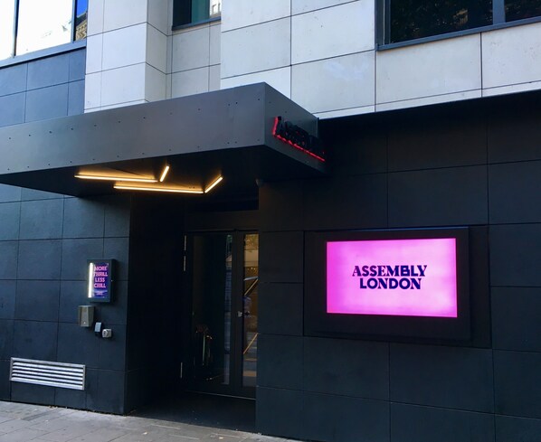 The exterior of a building with a neon sign reading "ASSEMBLY LONDON" and a modern entrance with a glass door. - Assembly Leicester Square (London)