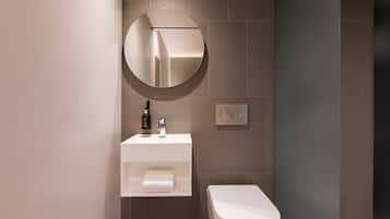 A modern bathroom with a white sink, a round mirror, a toilet, and a towel shelf.
