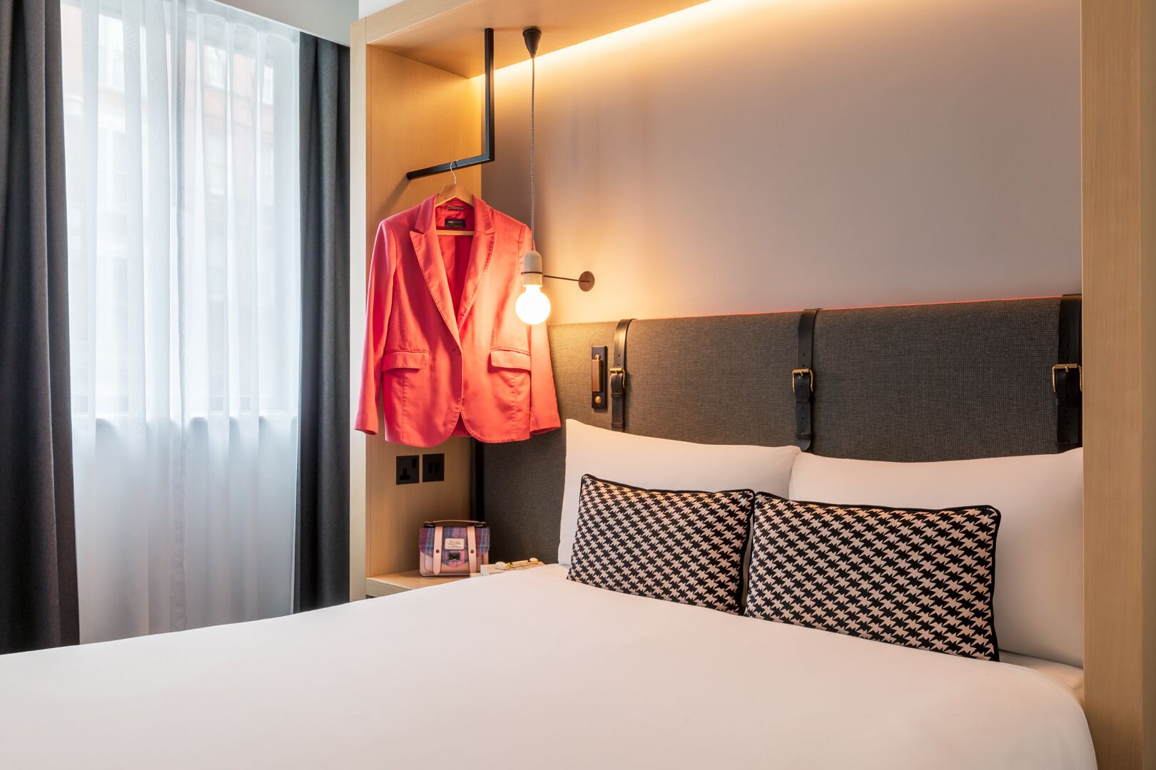 Una habitación de hotel con una cama, una bata colgada, una mesita de noche y una lámpara.