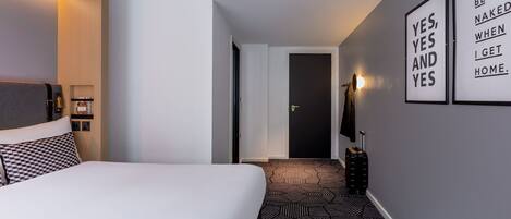 A hotel room with a large bed, a geometric patterned carpet, a black door, and motivational wall art.