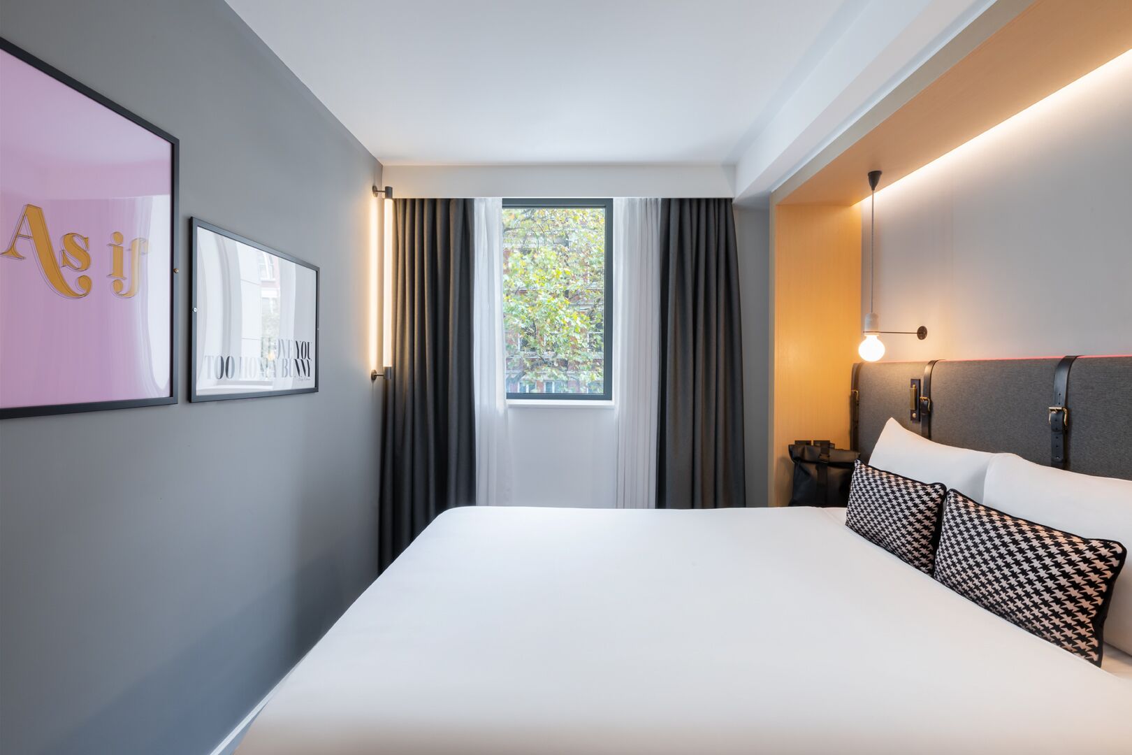 Een moderne hotelkamer met een groot bed, een raam met gordijnen, een wandlamp en ingelijste kunstwerken.