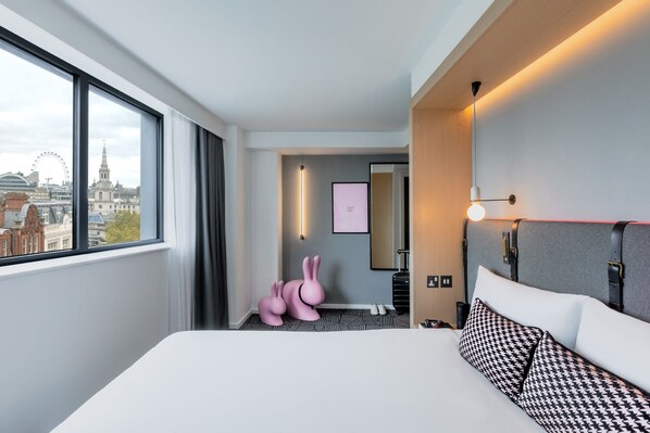 Hotelkamer met een groot bed, uitzicht op de stad, een spiegel, een wandlamp en een roze konijnenbeeldje.