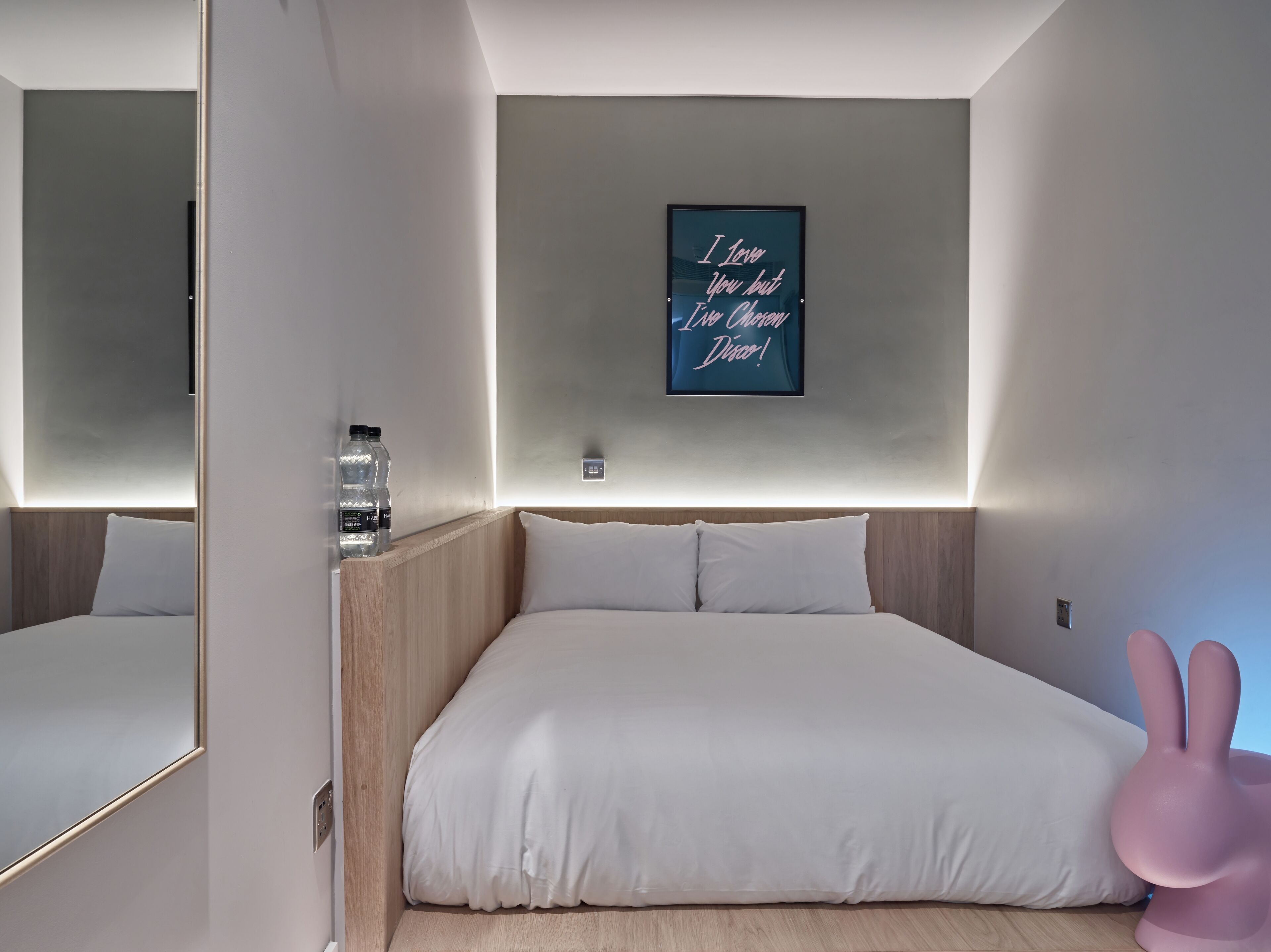 A modern bedroom with a large bed, a wall-mounted light, and a motivational quote.