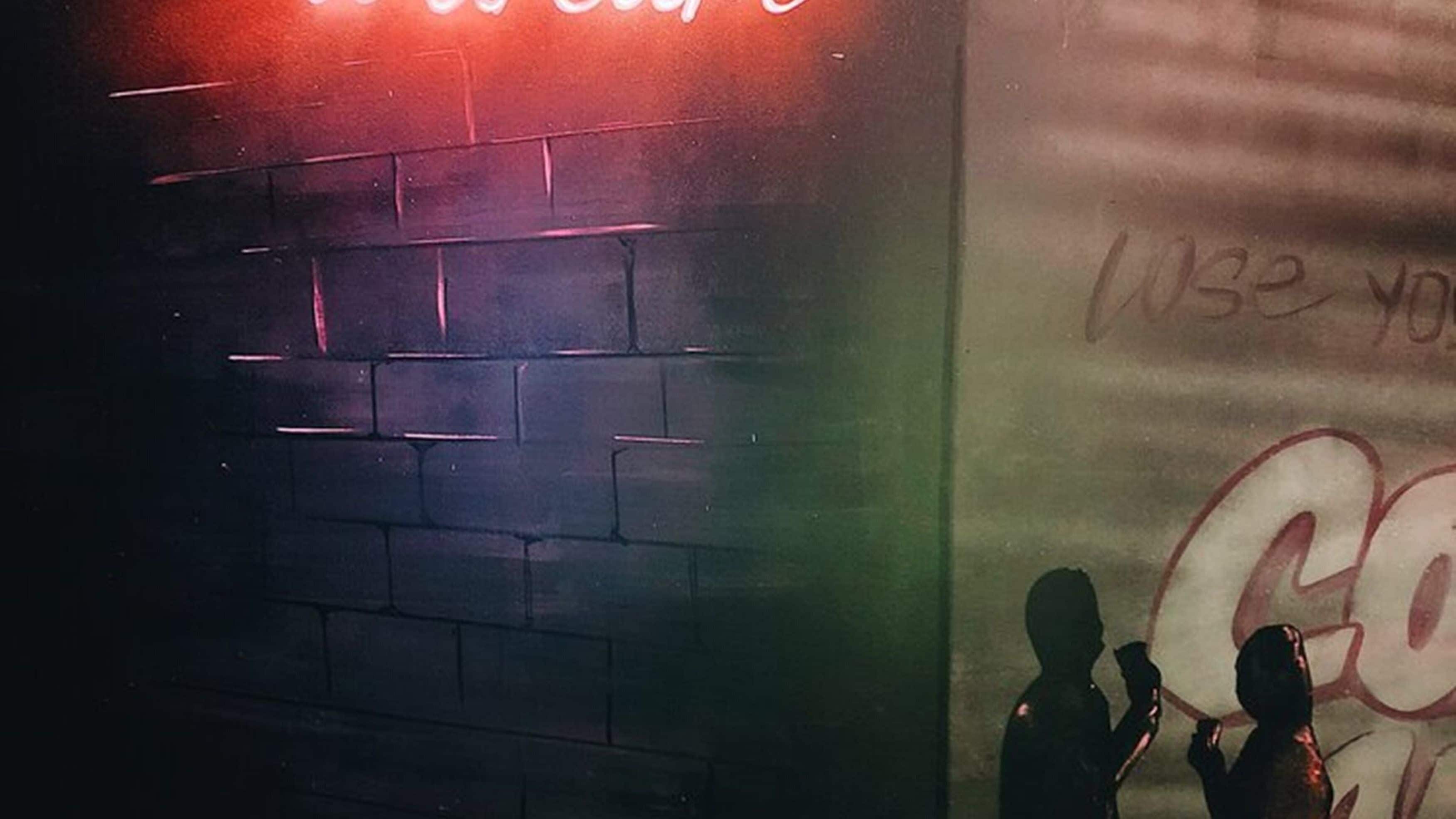 A brick wall with graffiti and a neon sign.