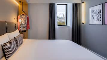 Une chambre d’hôtel avec un grand lit, une vue sur le paysage urbain par la fenêtre et un luminaire fixé au mur.