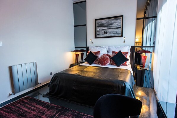 Habitación de hotel moderna con una cama grande, vistas al mar y un sofá de cuero negro.