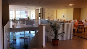 A spacious indoor area with a high ceiling, a seating area with tables and chairs, and a potted plant in the foreground. - Hotel Residence Santa Loja (Tito)