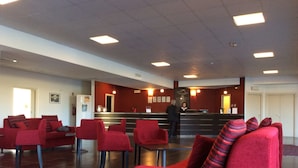 A hotel lobby with red seating, a reception desk, and a man standing near the counter. - Hotel Residence Santa Loja (Tito)