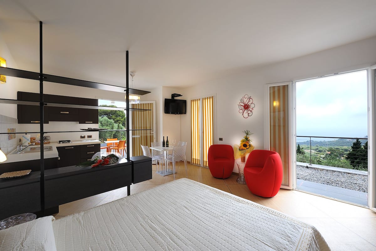 Ein modernes Schlafzimmer mit einem großen Bett, einem schwarzen Kleiderschrank, einem Essbereich mit Tisch und Stühlen sowie einem Balkon mit Aussicht.