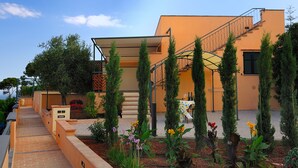 A modern building with a staircase, outdoor seating, and a garden with various plants. - Poggio dei Gorleri Wine resort (Diano Marina)