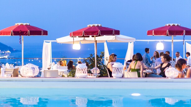 A poolside area with red umbrellas, lounge chairs, and tables set up for guests. - Poggio dei Gorleri Wine resort (Diano Marina)