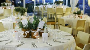 A banquet hall with round tables set for a formal event, featuring white tablecloths, glassware, and potted plants. - Poggio dei Gorleri Wine resort (Diano Marina)