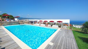 A swimming pool with a wooden deck, red umbrellas, and a view of the ocean. - Poggio dei Gorleri Wine resort (Diano Marina)