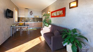 A modern living room with a sofa, a dining table with chairs, a kitchen in the background, and a potted plant. - Poggio dei Gorleri Wine resort (Diano Marina)