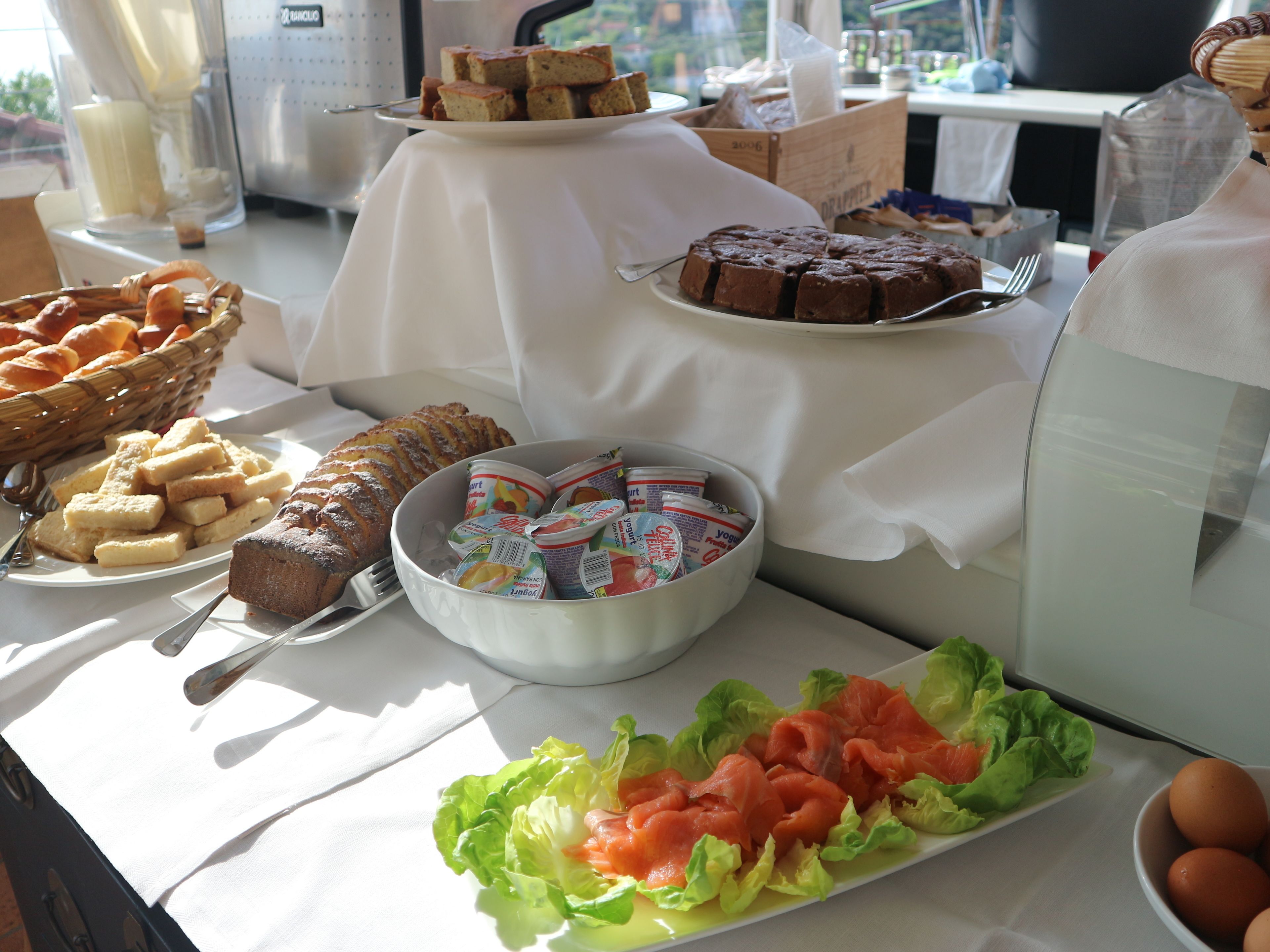 A buffet table with various food items including bread, cakes, yogurt, and fresh vegetables.