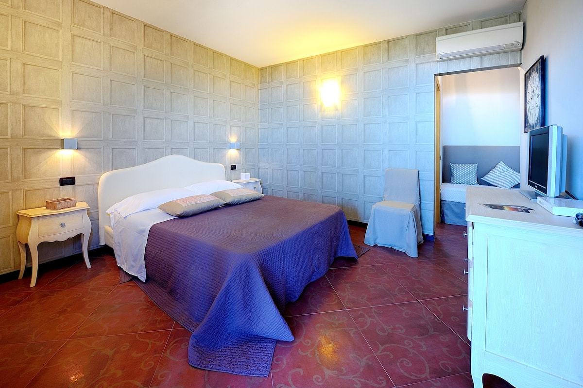 Ein Hotelzimmer mit einem großen Bett, Nachttischen, einem Schreibtisch und einem Fernseher.