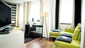 A modern living room with a flat-screen TV, a sofa, a desk, and a lamp. - City Hotel Bosse (Bad Oeynhausen)