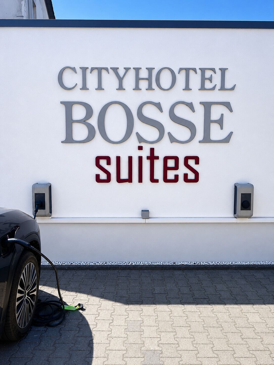 Una pared con el texto 'CITYHOTEL BOSSE suites' y una estación de carga para vehículos eléctricos.