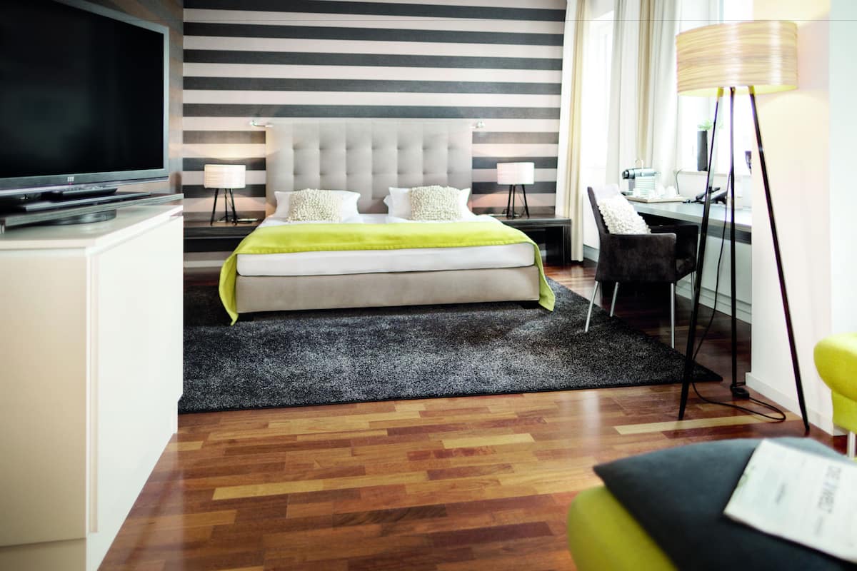 A modern hotel room with a large bed, a flat-screen TV, a desk with a chair, and a lamp.