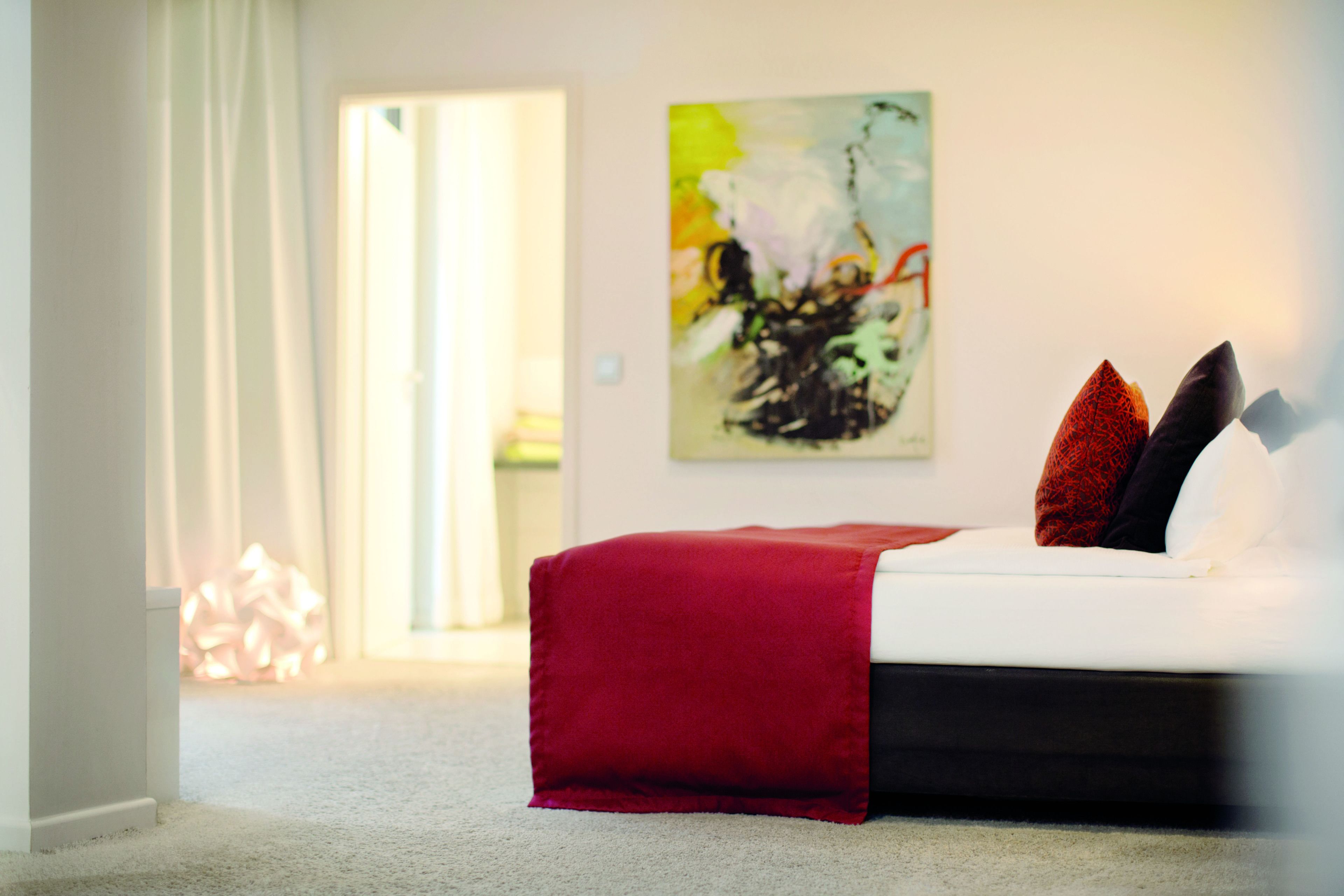 Une chambre à coucher avec un lit, un plaid rouge et un tableau accroché au mur.