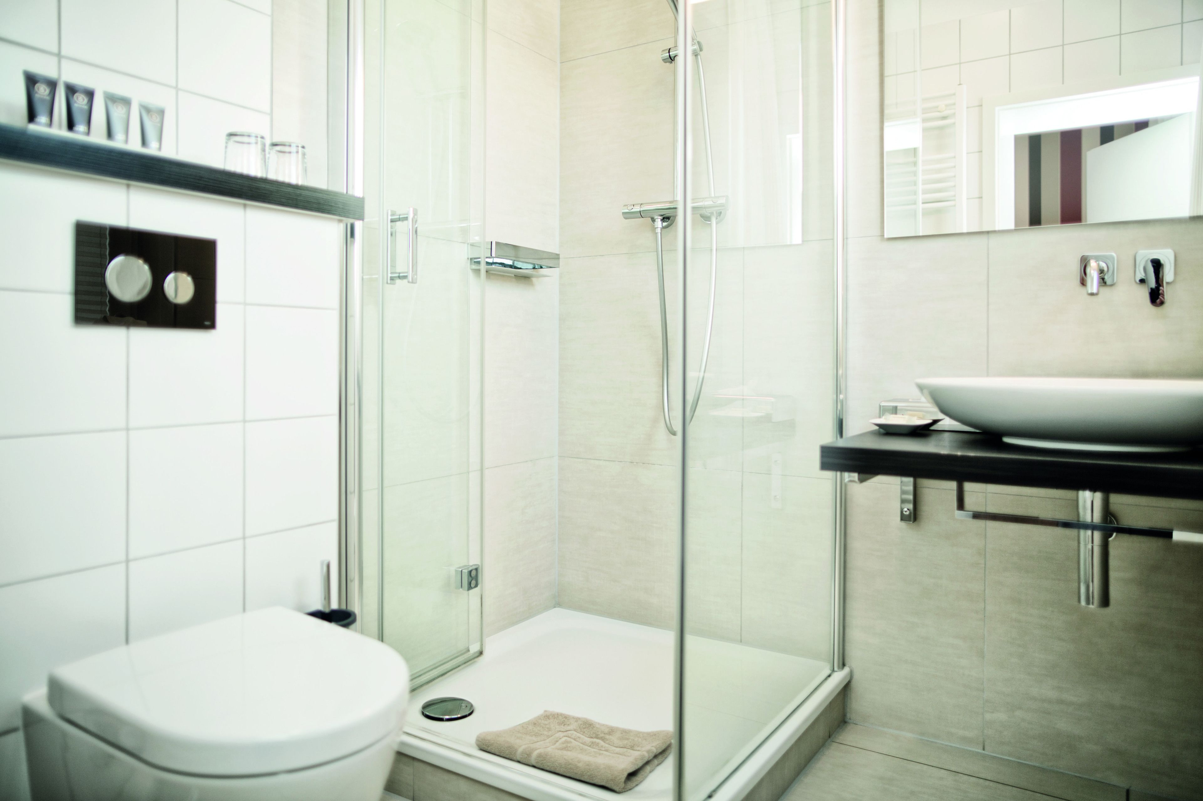 A modern bathroom with a glass-enclosed shower, a white toilet, and a sink with a mirror above it.