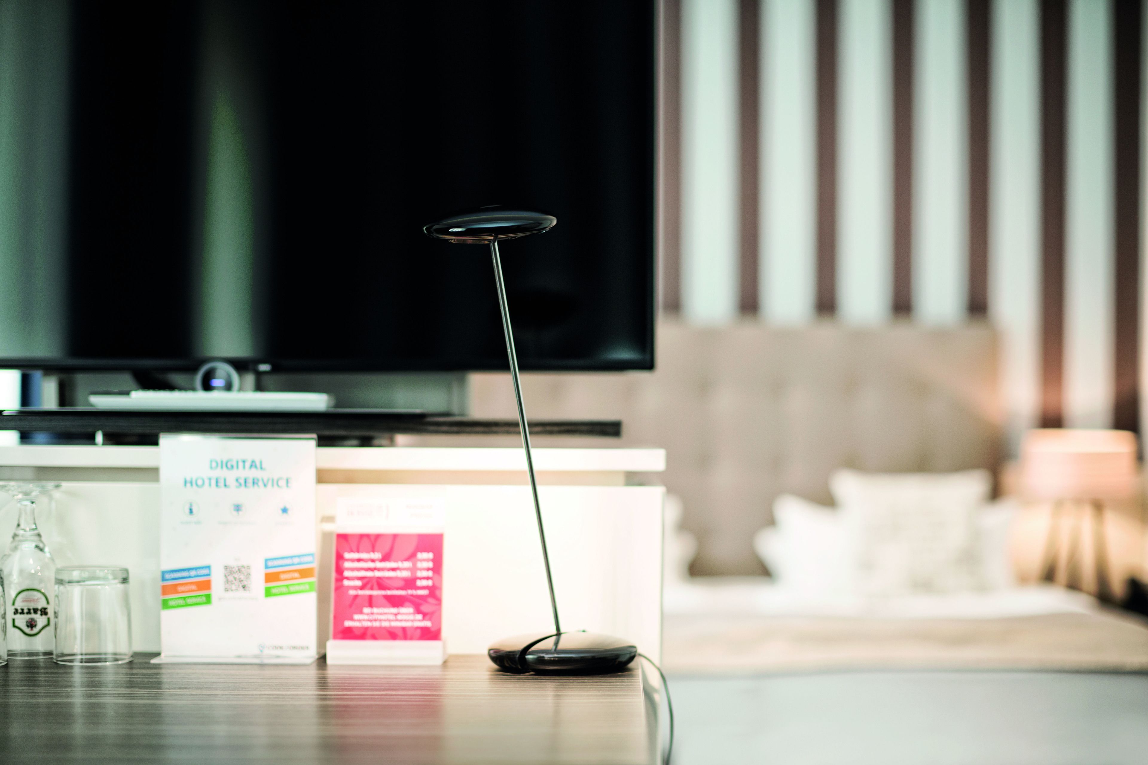 Habitación de hotel con televisor de pantalla plana, un panel de servicios digitales y un vaso de agua sobre la mesa.